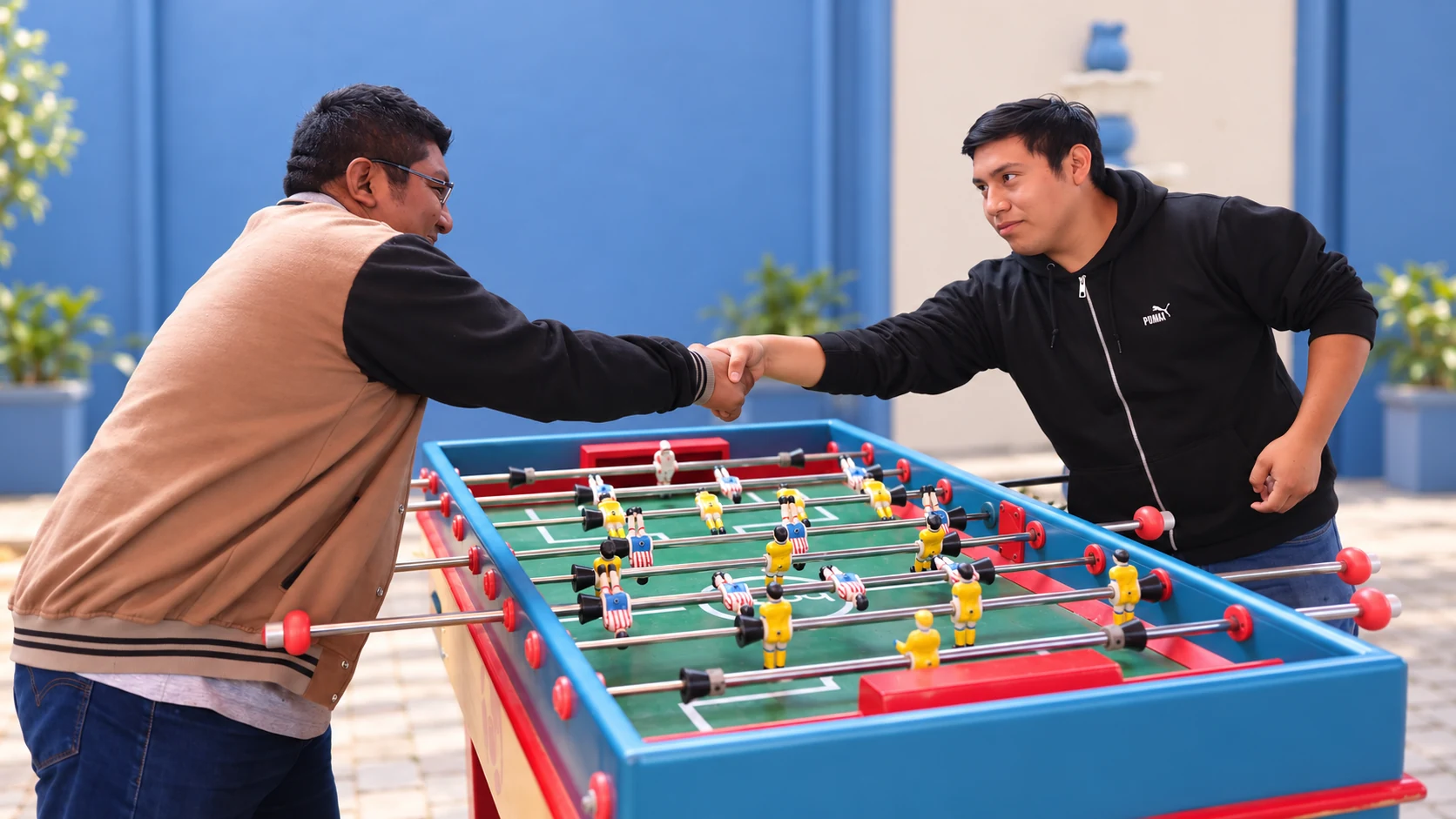 Dos estudiantes estrechan la mano junto al futbolito en el campus IUDY